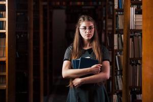 mira hacia la cámara. una estudiante está en una biblioteca llena de libros. concepción de la educación foto