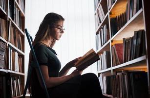 Sits and learning some new information. Female student is in library that full of books. Conception of education photo