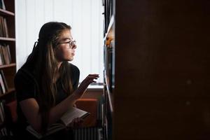 Searching for right information. Against window. Female student is in library that full of books. Conception of education photo