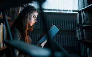 Getting smarter every day. Female student is in library that full of books. Conception of education photo