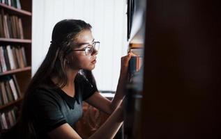 buscando información correcta. contra ventana. una estudiante está en una biblioteca llena de libros. concepción de la educación foto