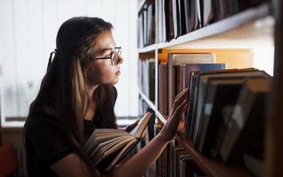 Searching for right information. Against window. Female student is in library that full of books. Conception of education photo