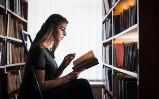 Sits and learning some new information. Female student is in library that full of books. Conception of education photo