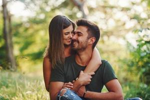 Sitting and embracing. Beautiful young couple have a good time in the forest at daytime photo