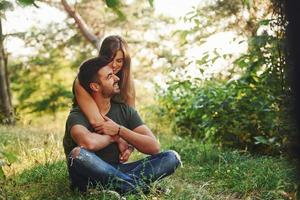 Sitting and embracing. Beautiful young couple have a good time in the forest at daytime photo