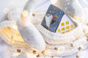 la acogedora casa está envuelta en un sombrero y una bufanda en una tormenta de nieve -decoración del alféizar de la ventana. invierno, nieve: aislamiento del hogar, protección contra el frío y el mal tiempo, sistema de calefacción de habitaciones. estado de ánimo festivo, navidad, año nuevo foto