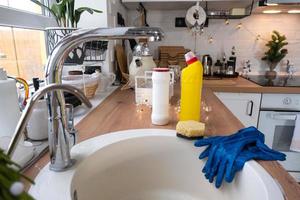 Cleaning the kitchen before the Christmas and New Year holidays. Detergent, dry powder, sponge, gloves are on the sink. Festive decor in the white kitchen, cozy interior of the home photo