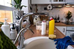 limpiar la cocina antes de las vacaciones de navidad y año nuevo. detergente, polvo seco, esponja, guantes en el fregadero. decoración festiva en la cocina blanca, acogedor interior de la casa foto