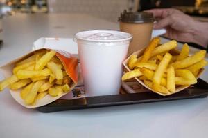 comida rápida en una bandeja en un restaurante. papas fritas, un vaso con batido, café foto