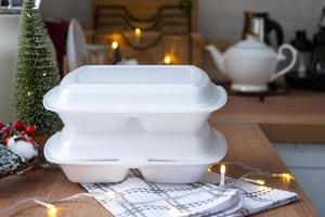 Food delivery service containers on table white scandi festive kitchen in christmas decor. Eve New year, saving time, too lazy to cook, hot order, disposable plastic box in fairy light. mock up photo