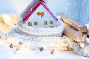 Cozy house is wrapped in a hat and scarf in a snowstorm -window sill decor. Winter, snow - home insulation, protection from cold and bad weather, room heating system. Festive mood, Christmas, New Year photo