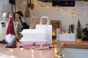 Food delivery service containers on table white scandi festive kitchen in christmas decor. Eve New year, saving time, too lazy to cook, hot order, disposable plastic box in fairy light. mock up photo