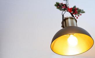 The black lampshade in the industrial loft style is decorated with spruce branches for Christmas and New Year on the background of fairy lights garlands. Close-up, minimalism photo