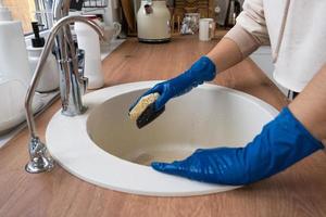 fregadero de limpieza en la cocina antes de las vacaciones de navidad y año nuevo. mano en guantes y esponja, detergente, polvo seco. decoración festiva en la cocina blanca, acogedor interior de la casa foto