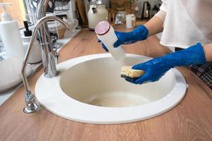 fregadero de limpieza en la cocina, mano en guantes y esponja, detergente, polvo seco. interior acogedor de la casa, restauración del orden, limpieza, desinfección foto