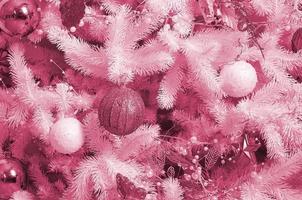 Decorating Christmas tree close up. Decoration bulb, white fir tree, golden x-mas toys and lights. Use for Christmas and New years celebration Image toned in Viva Magenta, color of the 2023 year photo