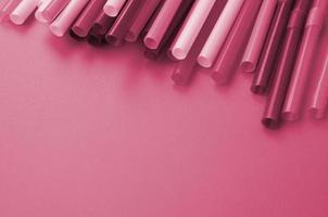 Many colorful straws for drinks lies on a bright orange background surface Image toned in Viva Magenta, color of the year photo