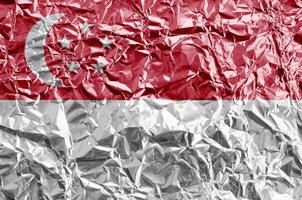 Singapore flag depicted in paint colors on shiny crumpled aluminium foil closeup. Textured banner on rough background photo