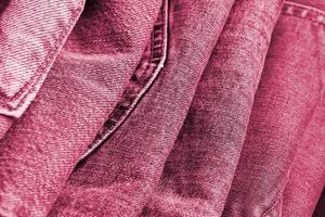 Many jeans in stack in wardrobe room. Row of pants denim jeans in closet. Concept of buy, sell, shopping and fashionable clothes Image toned in Viva Magenta, color of the 2023 year photo