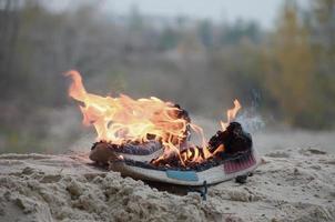 Burning sports sneakers or gym shoes on fire stand on sandy beach coast. Athlete burned out. Physical exertion during training concept photo