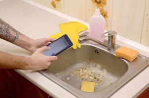 The landlord uses the tablet to call a cleaner in order to clean the clogged kitchen sink photo