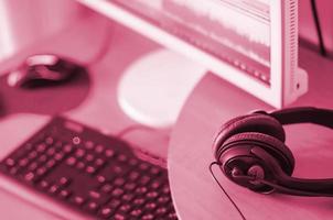 Big black headphones lie on the wooden desktop of the sound designer. Image toned in Viva Magenta, color of the 2023 year photo