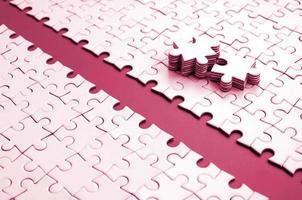 Path is laid on the platform of a white folded jigsaw puzzle. The missing elements of the puzzle are stacked nearby. Image toned in Viva Magenta, color of the 2023 year photo