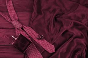 una botella de colonia masculina y gemelos con corbata azul se encuentran sobre un fondo de tela negra de lujo sobre una mesa de madera. imagen de accesorios para hombre tonificada en viva magenta, color del año 2023 foto