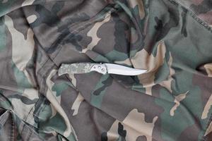 Military knife on army camouflage clothes close up. Background with copy space for military or special service design photo