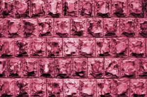 Texture design of the foundation or walls of buildings in the form of rectangular tiles made of solid granite stone with sharp corners Image toned in Viva Magenta, color of the 2023 year photo