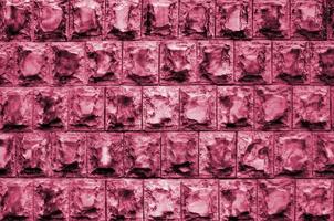 diseño de textura de los cimientos o paredes de edificios en forma de baldosas rectangulares hechas de piedra de granito sólido con esquinas afiladas imagen tonificada en viva magenta, color del año 2023 foto