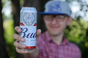 SUMY, UKRAINE - AUGUST 01, 2022 Young man raise Budweiser Bud beer can and shows BUD logo on blurred river and trees background. Budweiser is one of the most popular beer brands in the USA photo