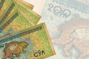 200 Uzbekistani som bills lies in stack on background of big semi-transparent banknote. Abstract business background photo