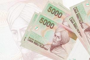 5000 Indonesian rupiah bills lies in stack on background of big semi-transparent banknote. Abstract presentation of national currency photo