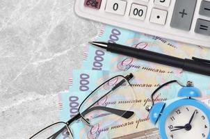 1000 Ukrainian hryvnias bills and calculator with glasses and pen. Business loan or tax payment season concept. Time to pay taxes photo