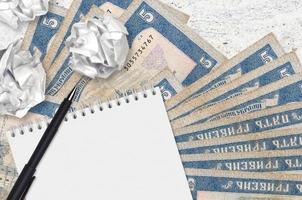 5 Ukrainian hryvnias bills and balls of crumpled paper with blank notepad. Bad ideas or less of inspiration concept. Searching ideas for investment photo