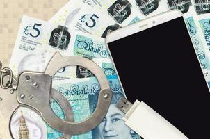 5 British pounds bills and smartphone with police handcuffs. Concept of hackers phishing attacks, illegal scam or malware soft distribution photo