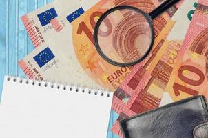 10 euro bills and magnifying glass with black purse and notepad. Concept of counterfeit money. Search for differences in details on money bills to detect fake photo