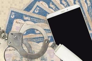 5 Ukrainian hryvnias bills and smartphone with police handcuffs. Concept of hackers phishing attacks, illegal scam or malware soft distribution photo