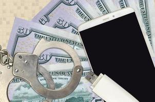 50 US dollars bills and smartphone with police handcuffs. Concept of hackers phishing attacks, illegal scam or malware soft distribution photo