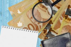 Billetes de 100 dólares canadienses y lupa con monedero negro y bloc de notas. concepto de dinero falso. busque diferencias en los detalles de los billetes de dinero para detectar falsos foto