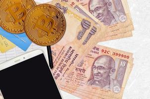 10 Indian rupees bills and golden bitcoins with smartphone and credit cards. Cryptocurrency investment concept. Crypto mining or trading photo