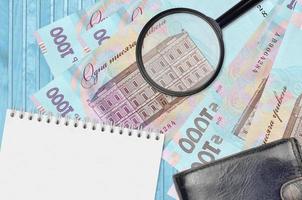 1000 Ukrainian hryvnias bills and magnifying glass with black purse and notepad. Concept of counterfeit money. Search for differences in details on money bills to detect fake photo