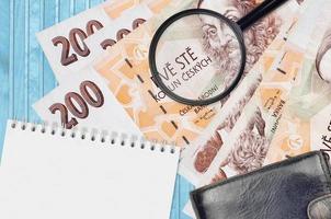 200 Czech korun bills and magnifying glass with black purse and notepad. Concept of counterfeit money. Search for differences in details on money bills to detect fake photo