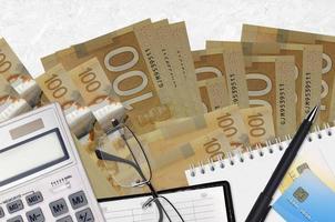Billetes de 100 dólares canadienses y calculadora con gafas y bolígrafo. concepto de pago de impuestos o soluciones de inversión. planificación financiera o papeleo contable foto