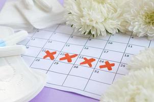 Menstrual pads and tampons on menstruation period calendar with white flowers on lilac background photo