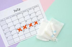 Flat lay composition with calendar and menstrual tampons and pad packs on blue pink and lilac pastel background photo