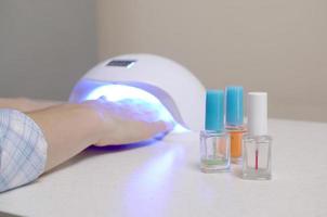 Three colorless transparent nail polish bottles in background of female hands in gel uv led nail white lamp for drying manicure photo