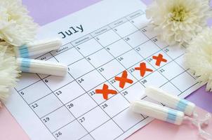 Menstrual tampons on menstruation period calendar with white flowers on lilac and pink background photo