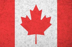 Canada flag depicted in bright paint colors on old relief plastering wall. Textured banner on rough background photo